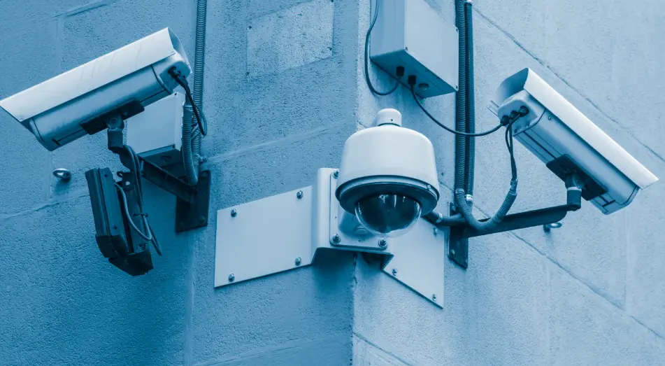 Drei professionelle Überwachungskameras an einer Hauswand — zwei Bullet-Kameras und eine PTZ-Dome-Kamera